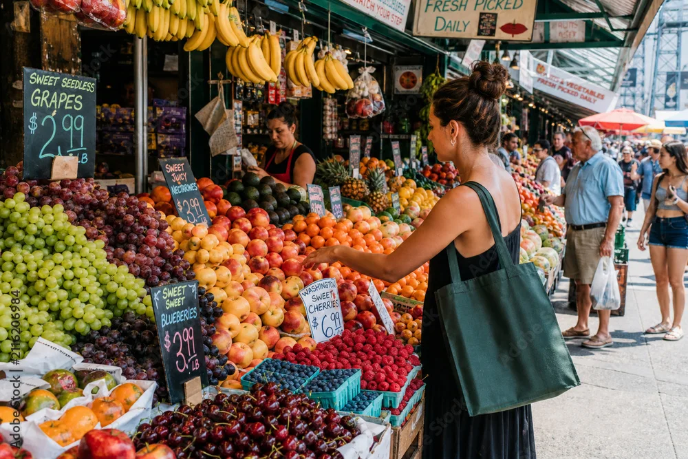 Shopper choosing fruit at a crowded outdoor market with price signs and rows of produce