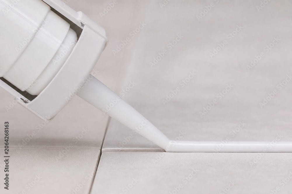 White caulk gun extruding a smooth bead of sealant into a tile joint